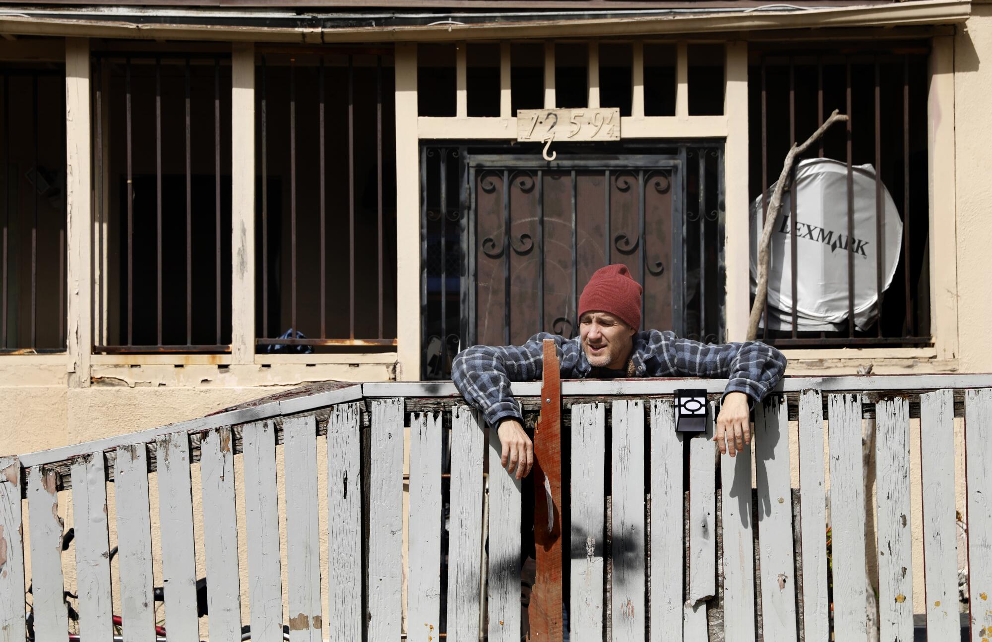 A man stands behind a fence between two apartment complexes. 