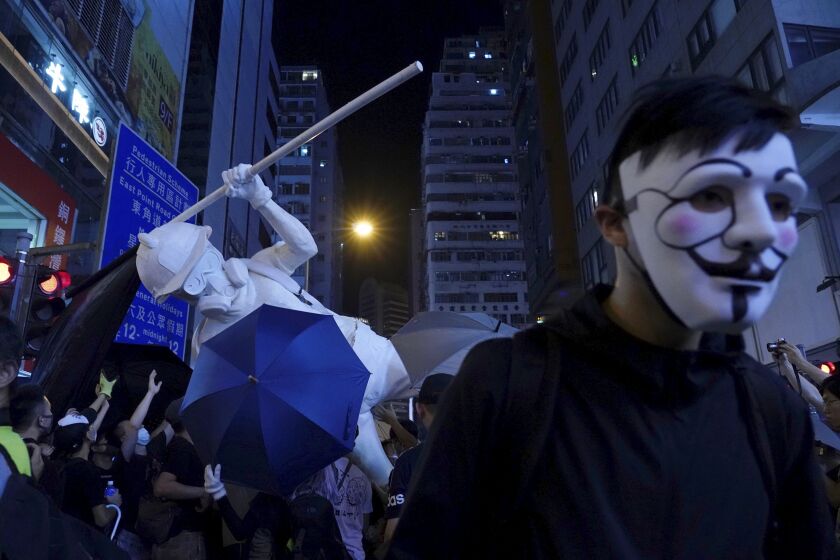 A protester with a mask stands near other protesters moving a statue depicting a protester armed with gas mask, helmet and umbrella on the streets of Hong Kong on Friday, Oct. 4, 2019. Masked protesters streamed into Hong Kong streets Friday after the city's embattled leader invoked rarely used emergency powers to ban masks at rallies in a hardening of the government's stance after four months of anti-government demonstrations. (AP Photo/Vincent Yu)