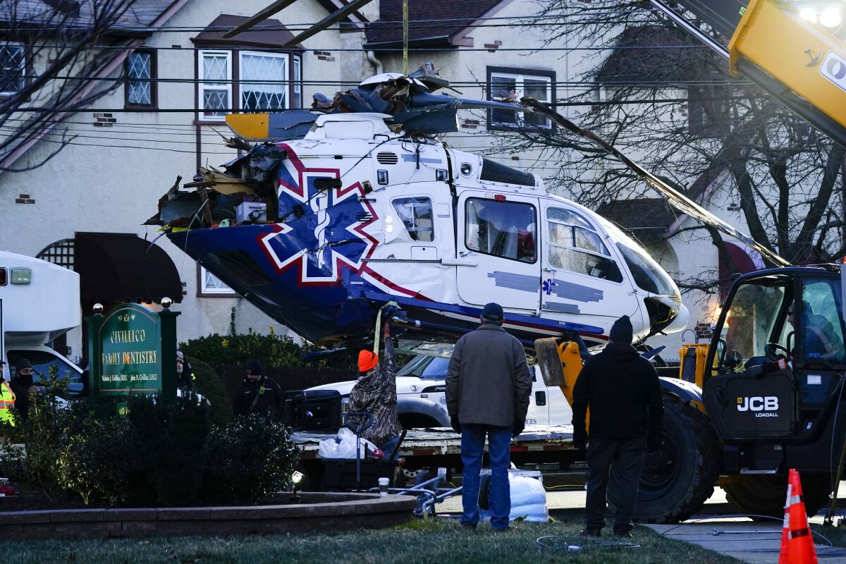 A crashed medical helicopter is removed from the scene in the Drexel Hill section of Upper Darby, Pa., on Wednesday, Jan. 12, 2022. Authorities and a witness say a pilot crash landed a medical helicopter without casualties in a residential area of suburban Philadelphia, miraculously avoiding a web of power lines and buildings as the aircraft fluttered, hit the street and slid into bushes outside a church. (AP Photo/Matt Rourke)