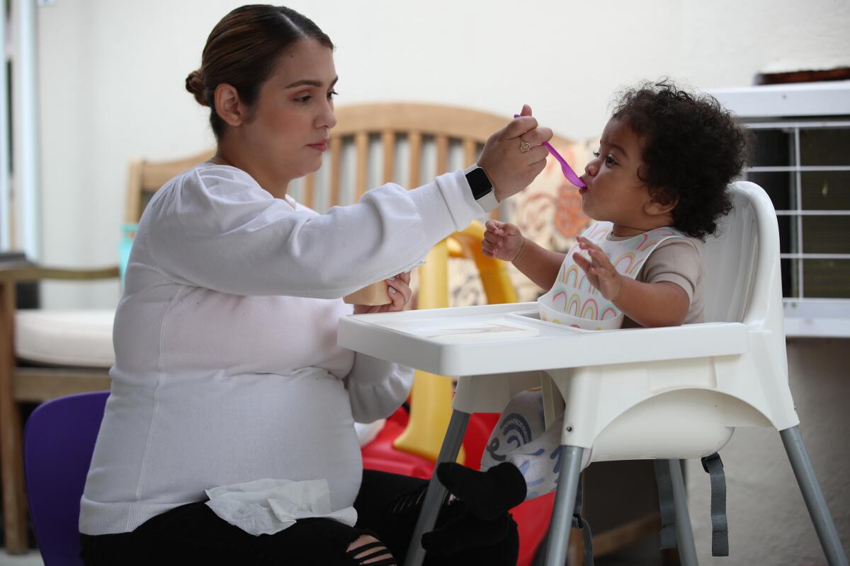 A woman feeds an infant in a high chair