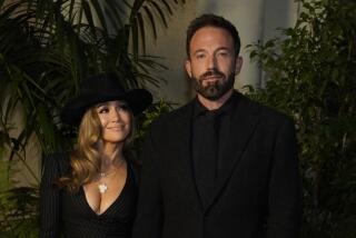 Jennifer Lopez in a black hat, plunging black dress looking at Ben Affleck in a black suit