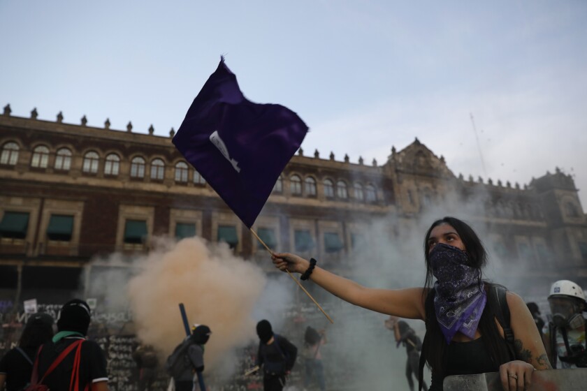 A woman waves a feminist flag as demonstrators attempt to storm the National Palace during a march to commemorate International Women's Day and protesting against gender violence, in Mexico City, Monday, March 8, 2021. (AP Photo/Rebecca Blackwell)