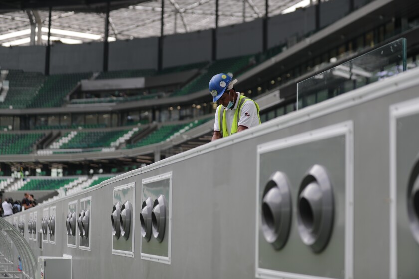 FILE - In this Dec. 15, 2019, file photo, a worker cleans above air conditioning vents at Qatar Education Stadium, an open cooled stadium with a 45,350-seat capacity, and one of the 2022 World Cup stadiums, in Doha, Qatar. Addressing airborne threats like the novel coronavirus is a particular challenge, especially when they can stick around for hours wherever they might land. The good news is many venues already use high-efficiency filtration that can capture most virus particles and keep them from spreading. The bad news is even the world’s most effective HVAC systems can’t do anything about the germs fans might touch on a railing or catch from a cough down the row. (AP Photo/Hassan Ammar, File)