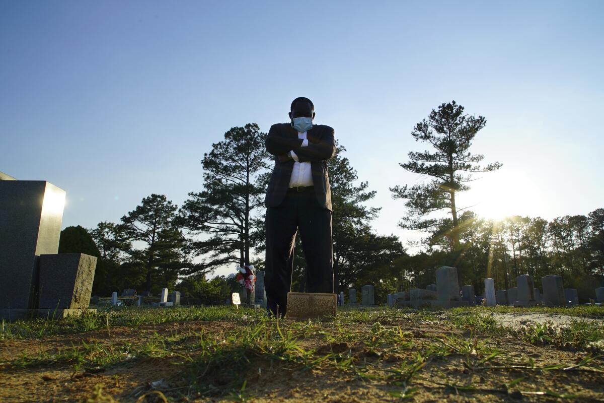 Mortician Shawn Troy stands at the grave of his father, William Penn Troy Sr., at Hillcrest Cemetery outside Mullins, S.C., on Sunday, May 23, 2021. The elder Troy, who developed the cemetery, died of COVID-19 in August 2020, one of many Black funeral directors to succumb during the pandemic. “I don’t think I’ll ever get over it,” he said. “But I’ll get through it.” (AP Photo/Allen G. Breed)