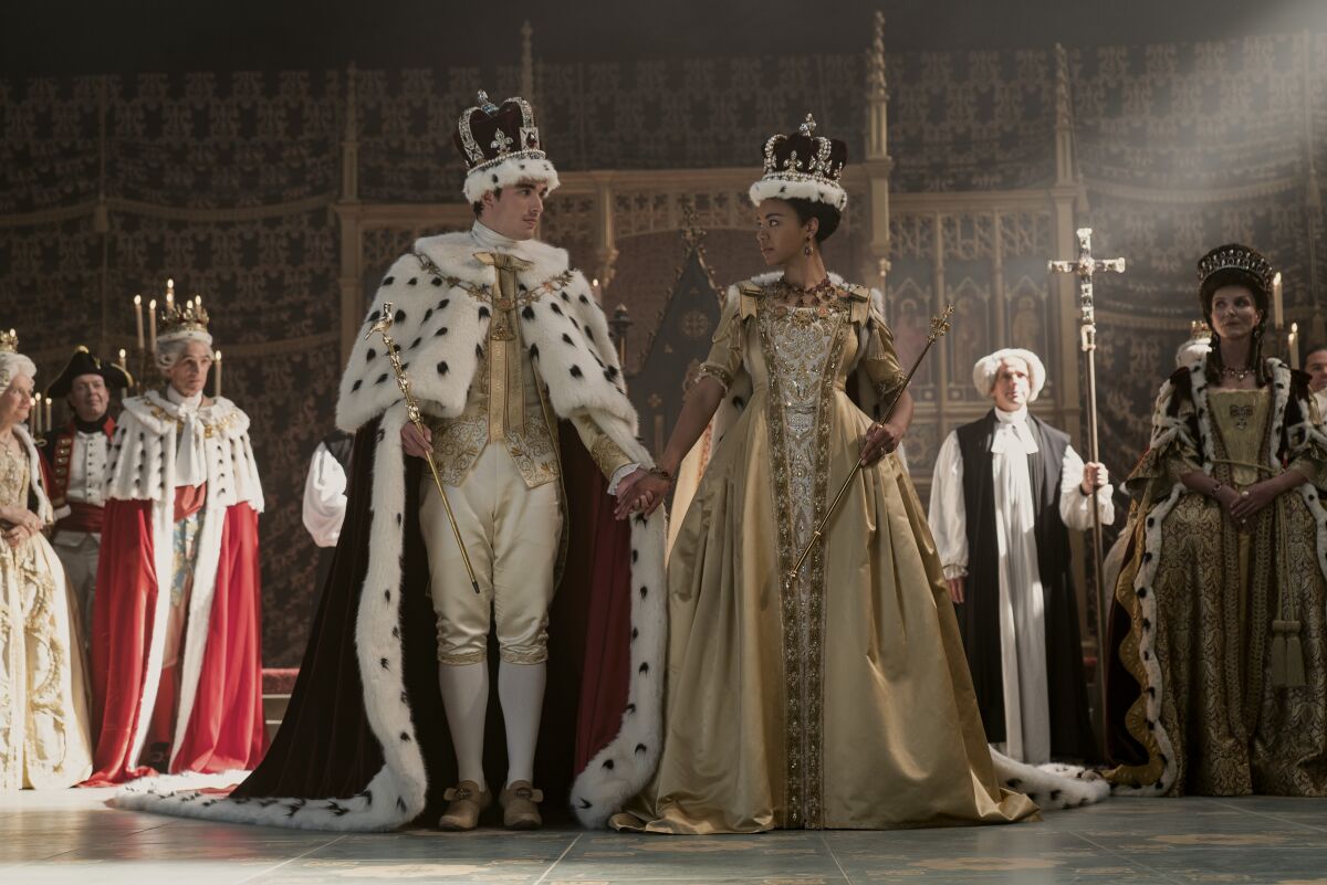 King George and Queen Charlotte are standing and holding hands, gazing at one another.
