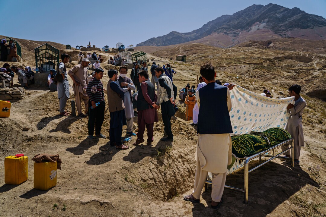 Relatives hold a sheet over a body at a funeral.