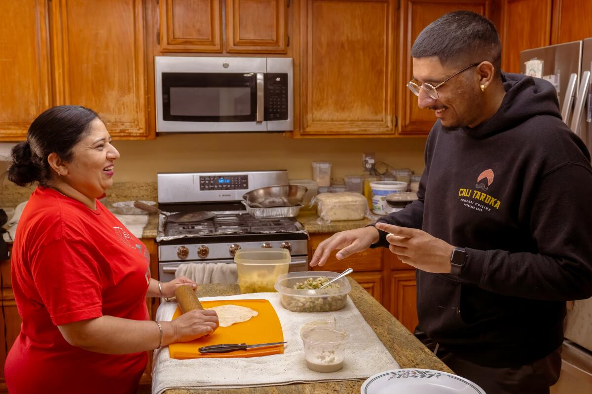 A mother and son stand cooking and laughing in their kitchen.