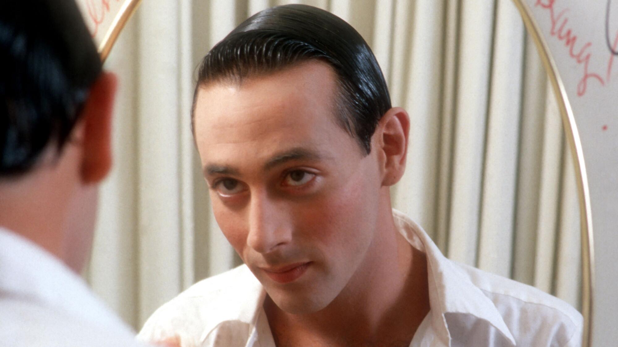 Paul Reubens looks at a reflection of his face in a mirror.