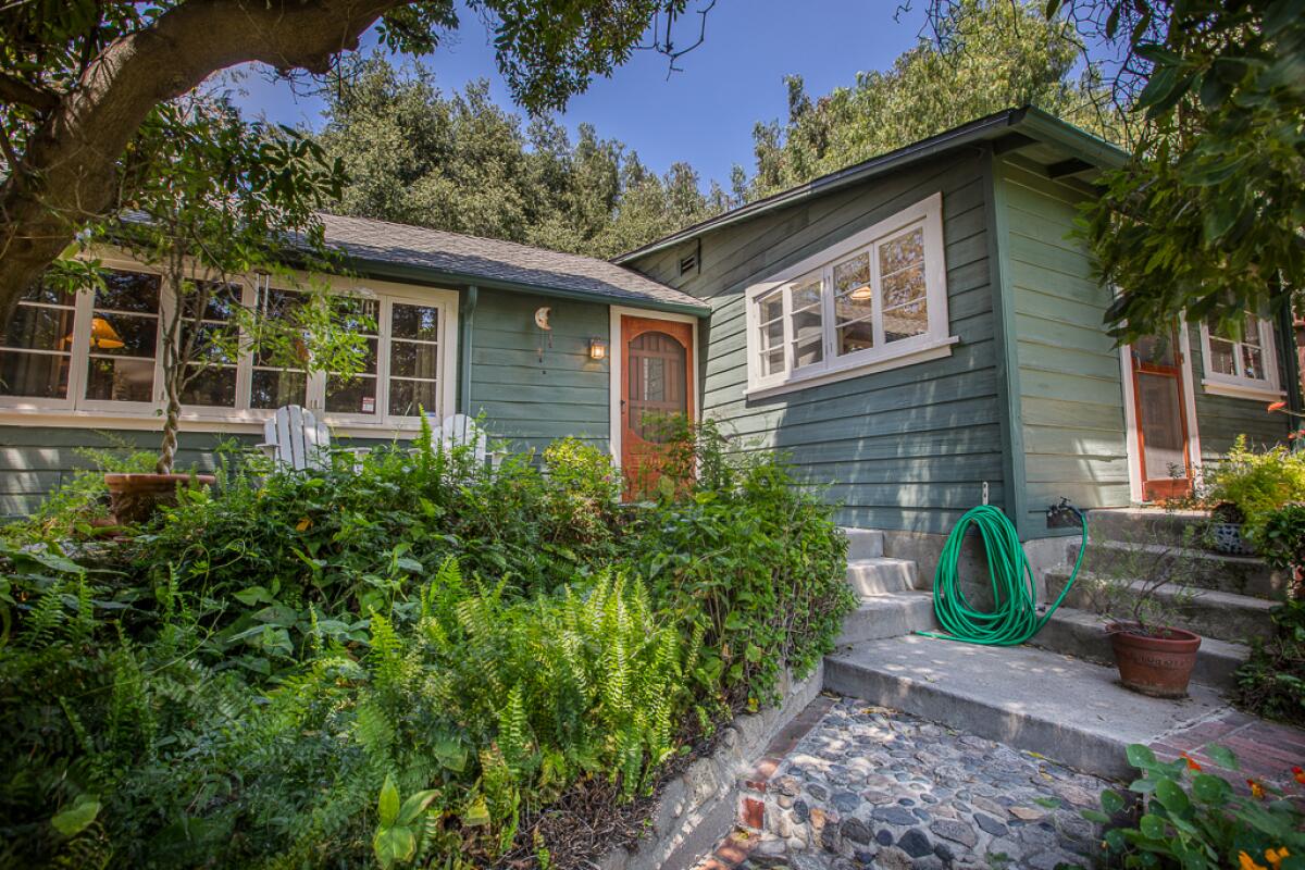 A modest one-story home, amid trees, with steps leading up to two entrances.