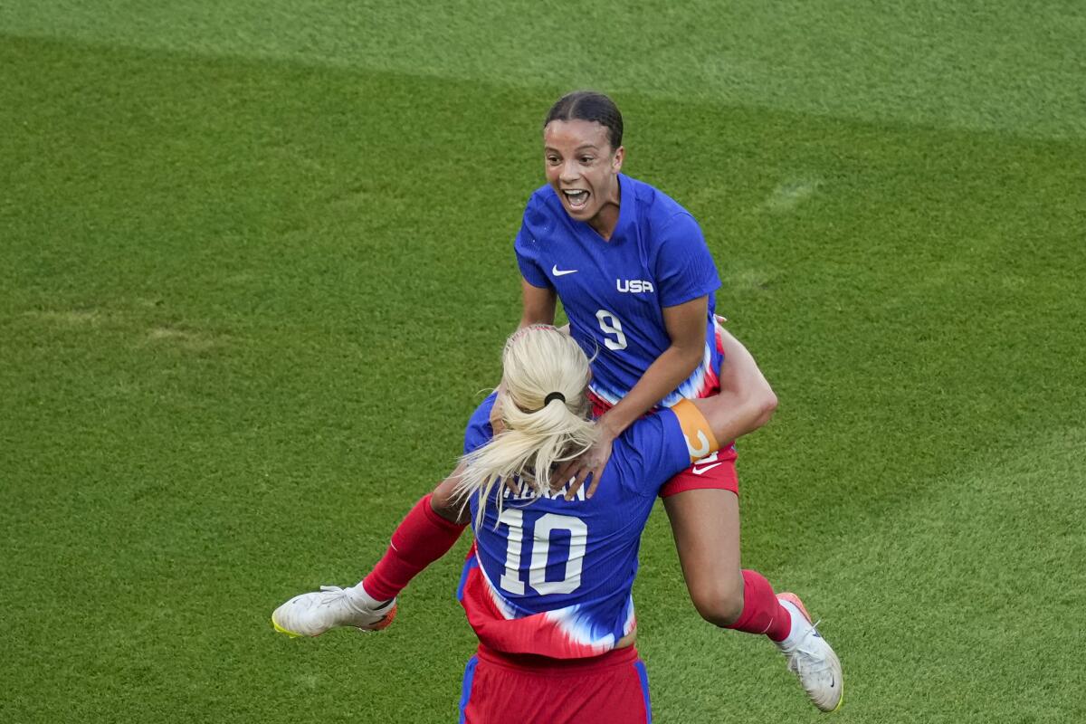 U.S. forward Mallory Swanson jumps up in front of teammate Lindsey Horan, who hugs her waist.