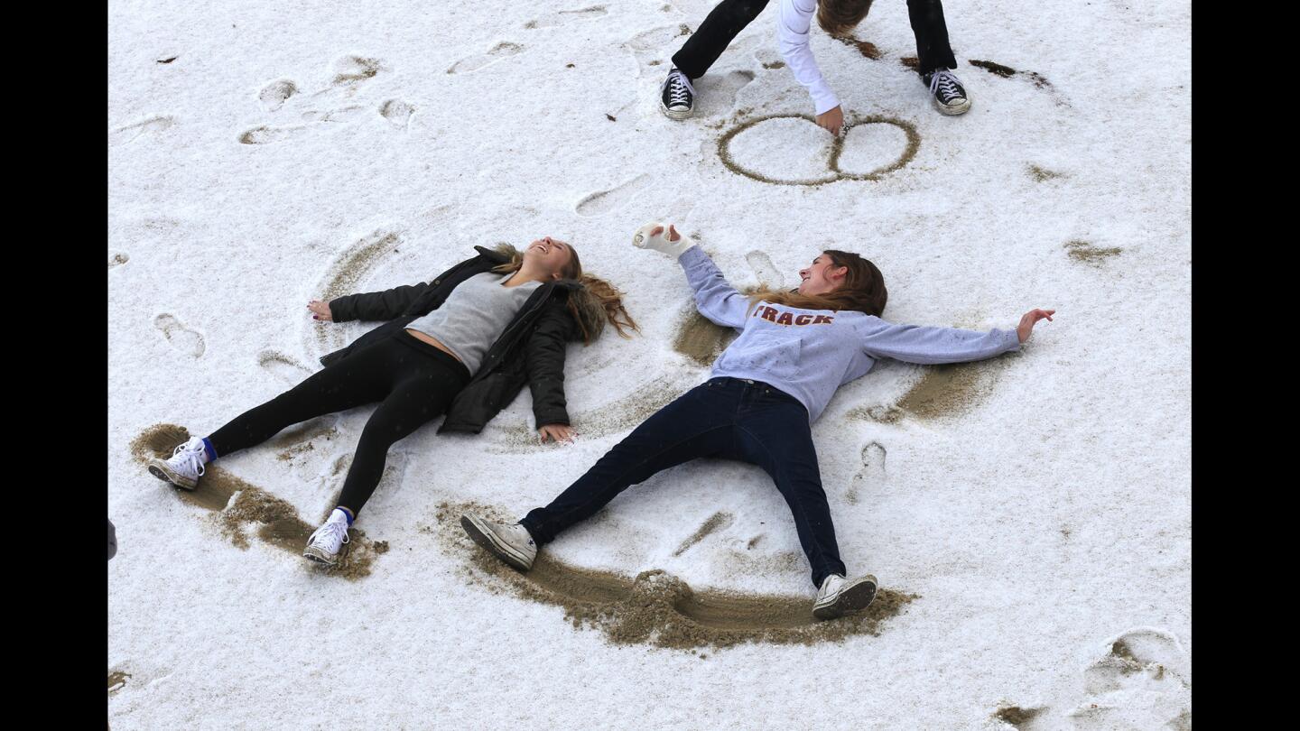 Youngsters make snow angels on a hail-covered beach in Huntington Beach.
