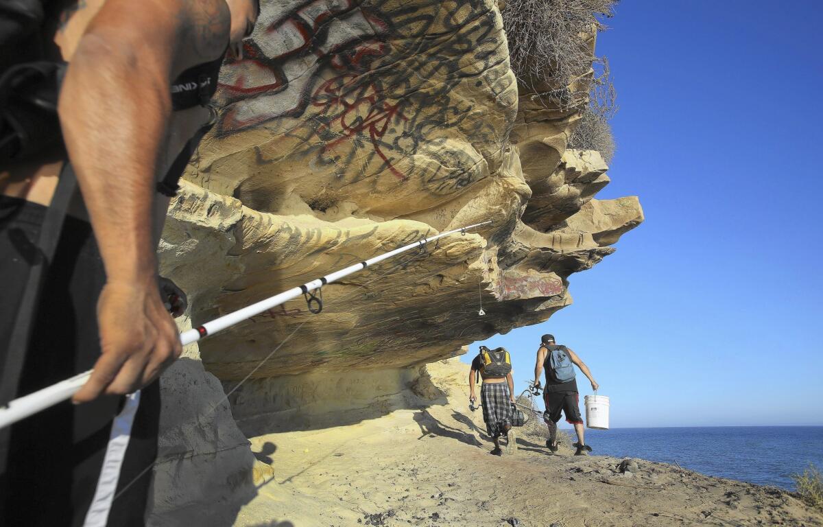 From left, Steven Navarro, Ramon Cardenas and Carlos Ramirez, all of Santa Barbara, pass a small cave at More Mesa after fishing from the shoreline below.