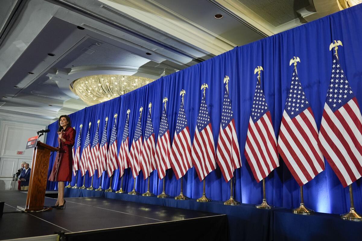 A woman speaks in front of a row of U.S. flags.