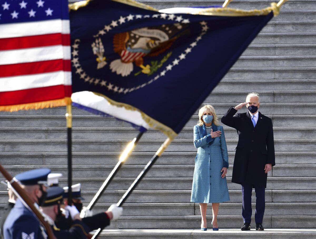 President Biden salutes as his wife, Jill Biden, puts her hand over her heart as troops pass them. 
