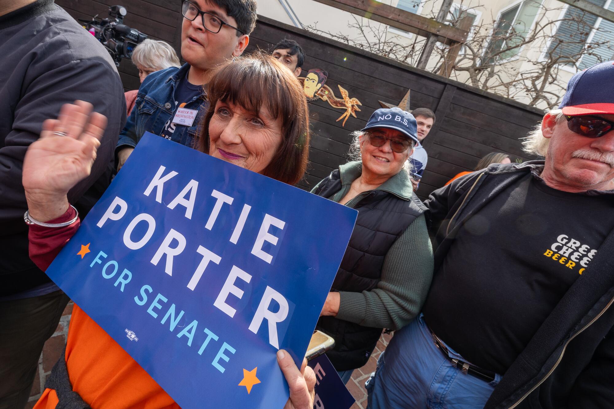 A woman at a rally holds a sign that says, "Katie Porter for Senate"