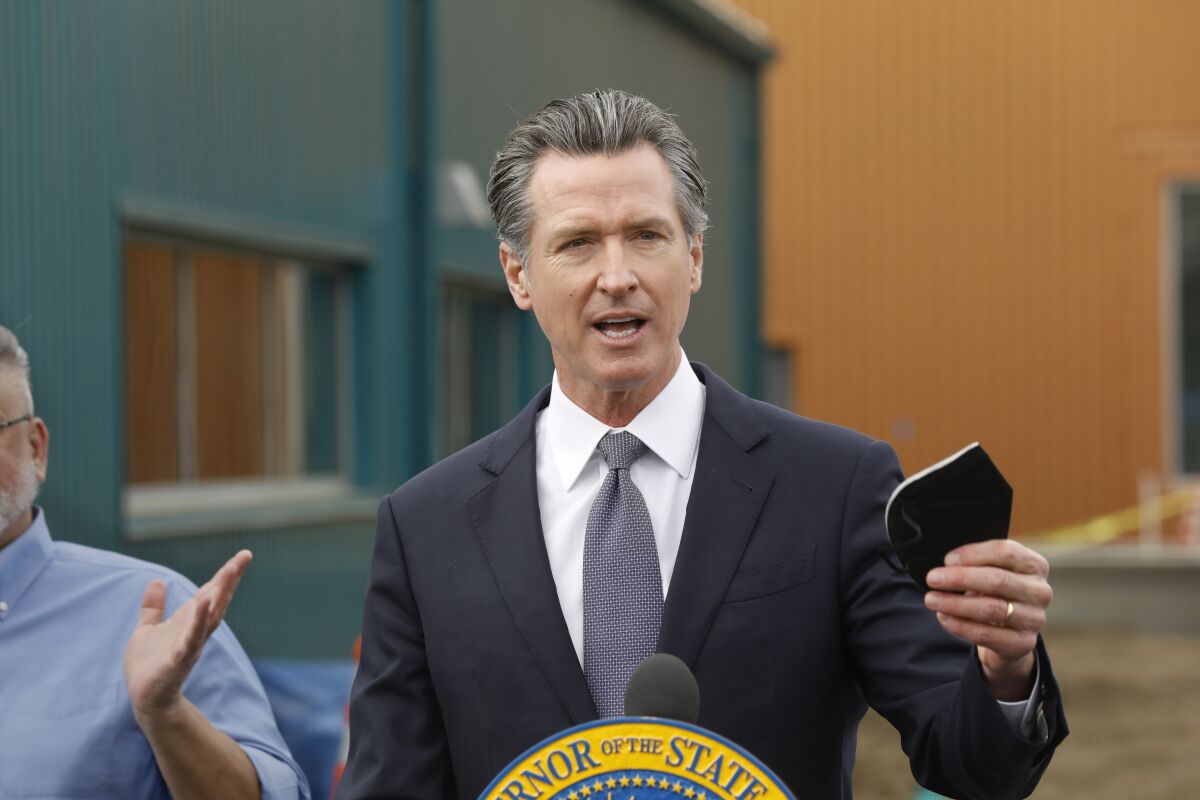 Gov. Gavin Newsom holding up a protective mask while speaking at an outdoor event