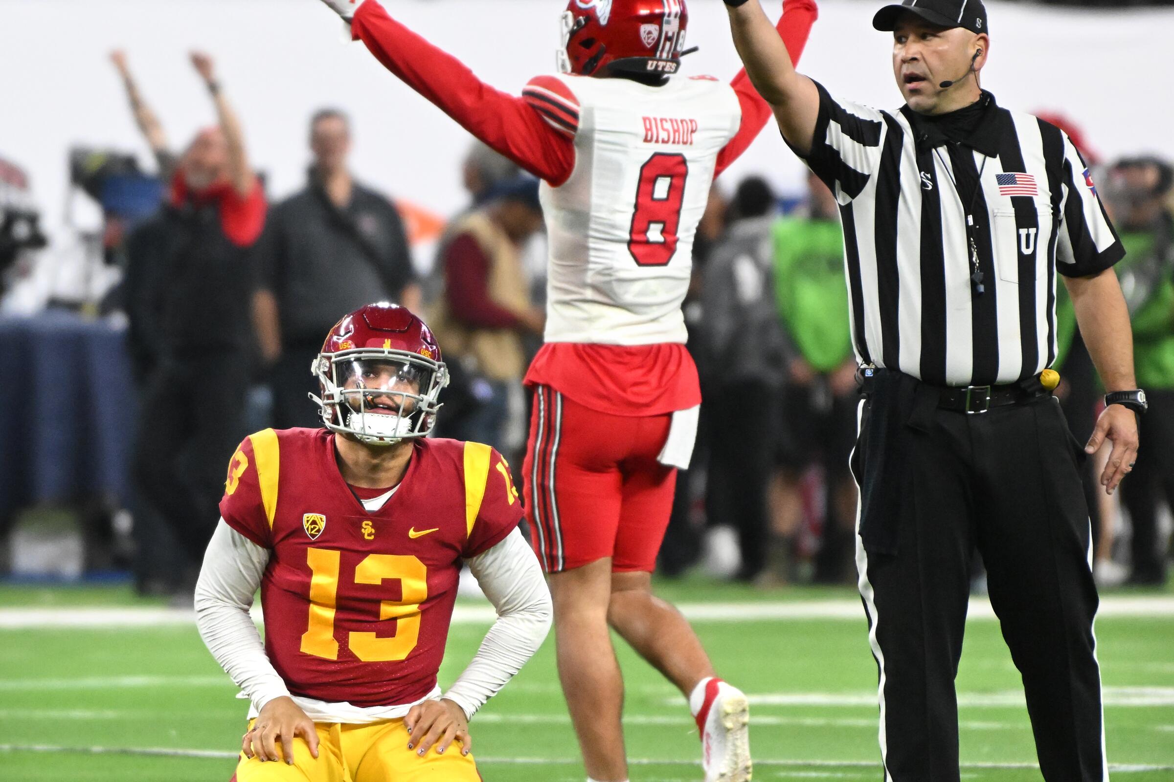 USC quarterback Caleb Williams kneels and Utah safety Cole Bishop holds his arms up while a referee points.