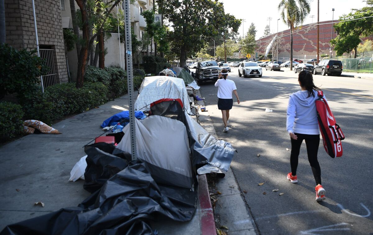 People walk past a row of tents lining a block in Los Angeles.