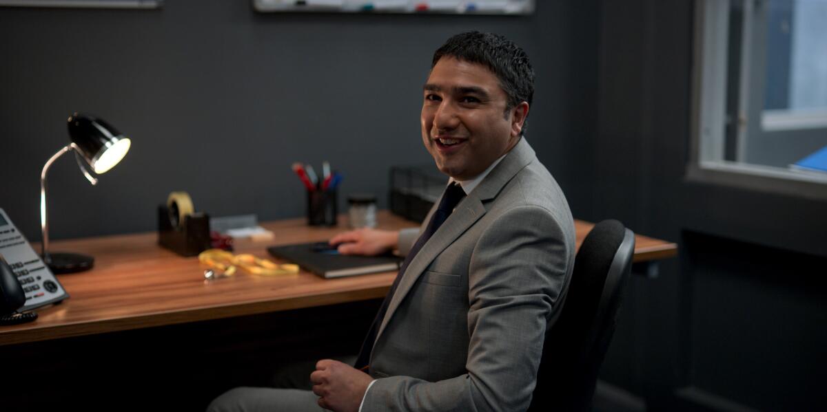 A man sitting at a desk in a suit smiling