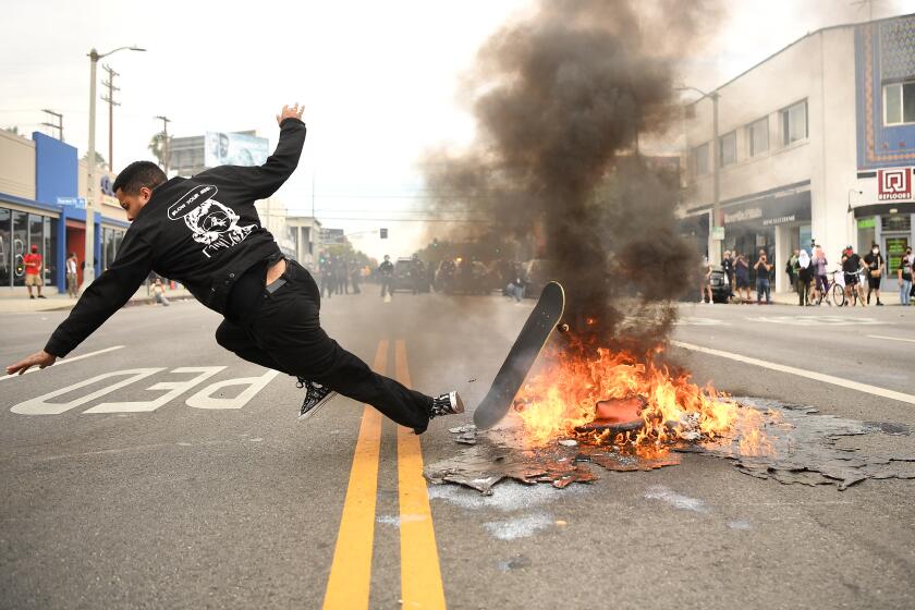 A skateboarder falls over a small fire set by protestors n 3rd St. in Los Angeles Saturday.