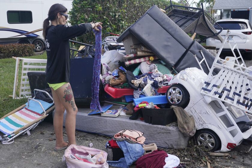 Alice Pujols goes through someone else's discarded items for clothes and shoes for her family Monday, Oct. 3, 2022, in Fort Myers, Fla. Pujols's home was completely destroyed after her home flooded due to rising waters caused by Hurricane Ian. (AP Photo/Marta Lavandier)