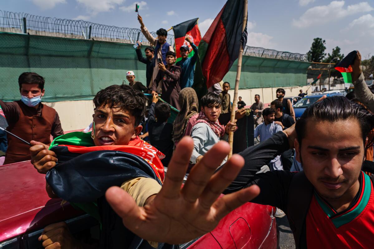 People march in the street carrying red, green and black Afghan flags.