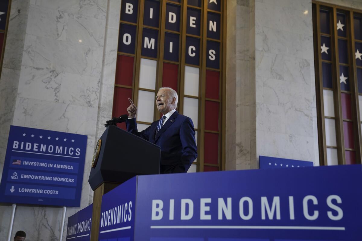 President Biden delivering a speech surrounded by signs reading 'Bidenomics'