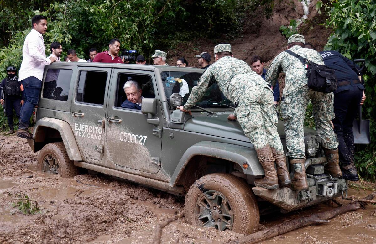 A man looks out the passenger's window of a jeep stuck in the mud, as others, some in military uniforms, stand on the vehicle