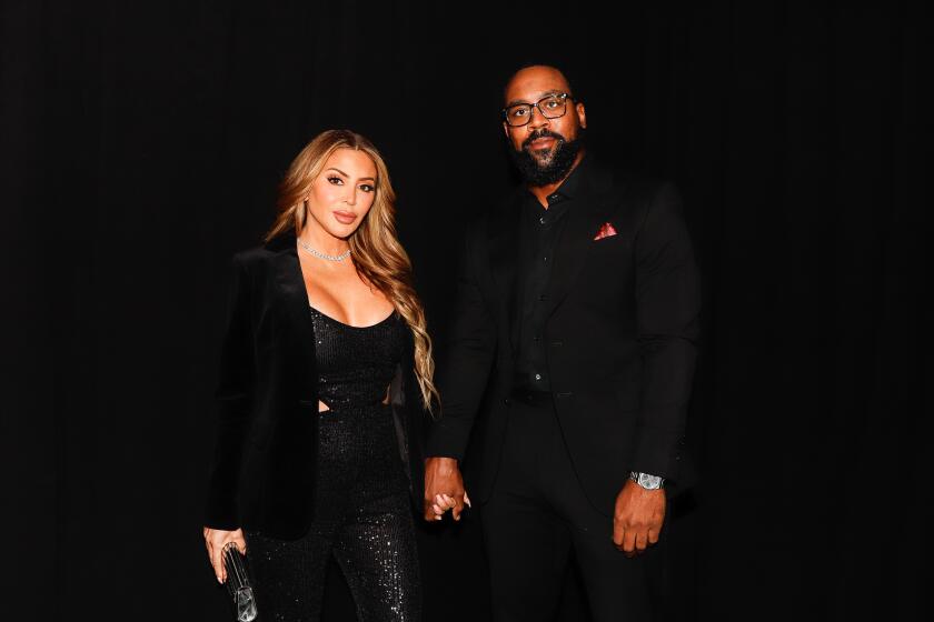 A woman with light brown hair in a black outfit holding hands with a Black man in glasses and a black outfit