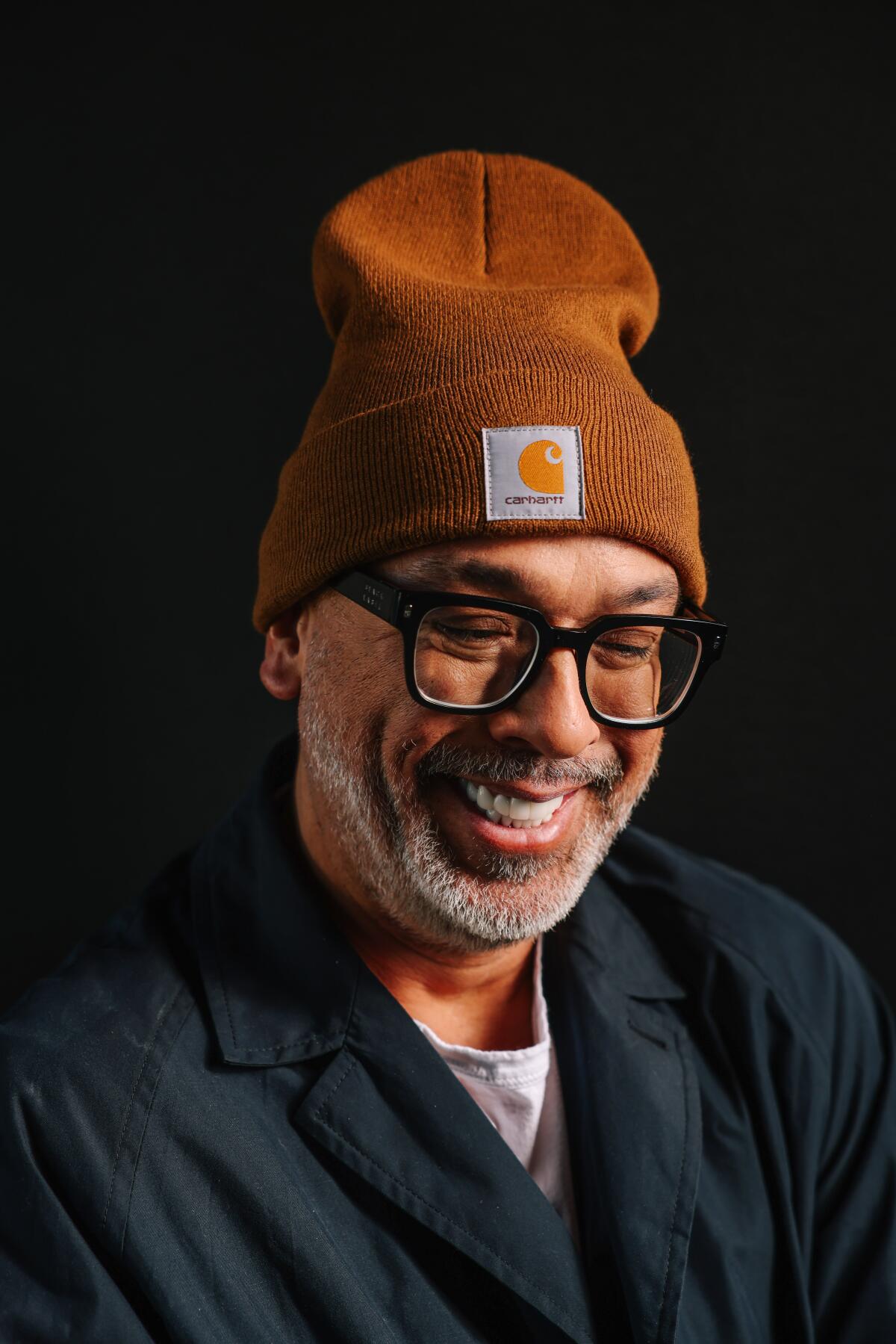 A man wearing a beanie and glasses smiles.
