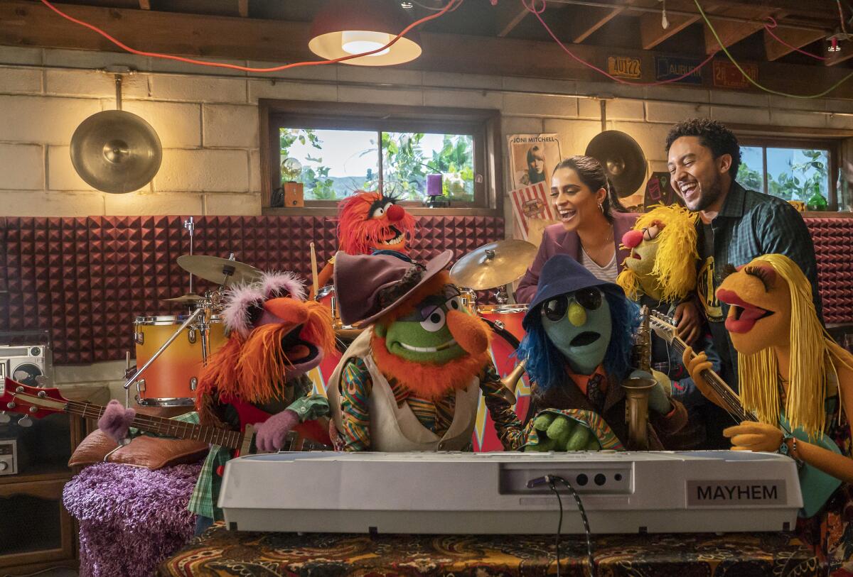 a group of muppets and two humans crowd around a keyboard 