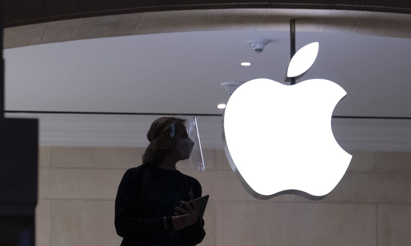 A person in a mask and carrying a computer is shown in silhouette near the Apple company logo.