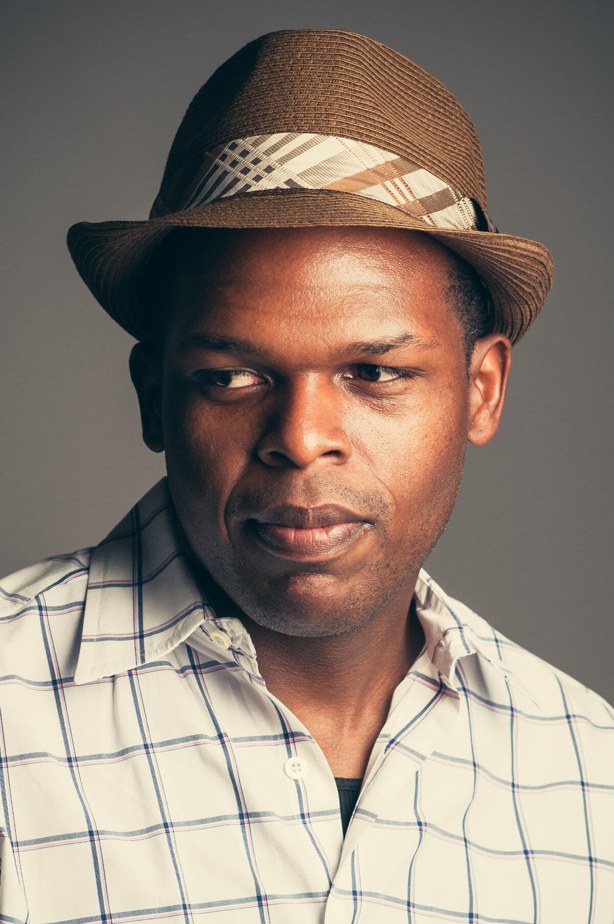 Maurice Carlos Ruffin, wearing a checked shirt and a brown hat.