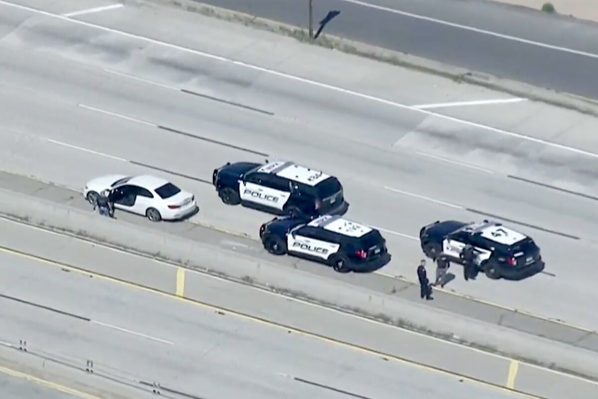 A white BMW and three police cruisers are parked on the 10 Freeway.
