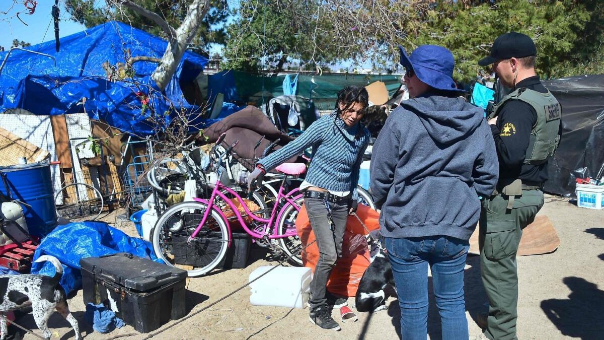 An officer from the Sheriff's Department and a social worker speak with a woman at the homeless encampment beside the Santa Ana River in Anaheim on Feb. 20.