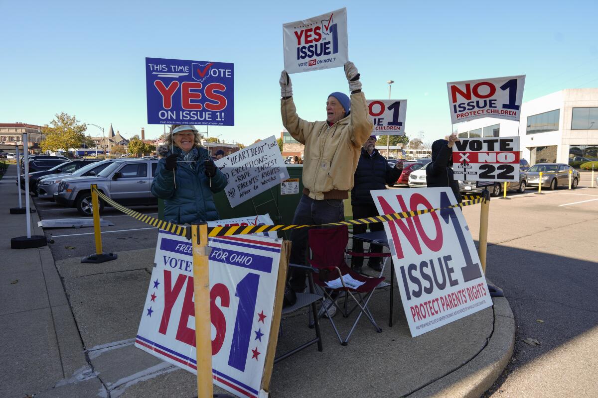 People in a parking lot hold signs reading "Vote Yes on 1" and "No on Issue 1."