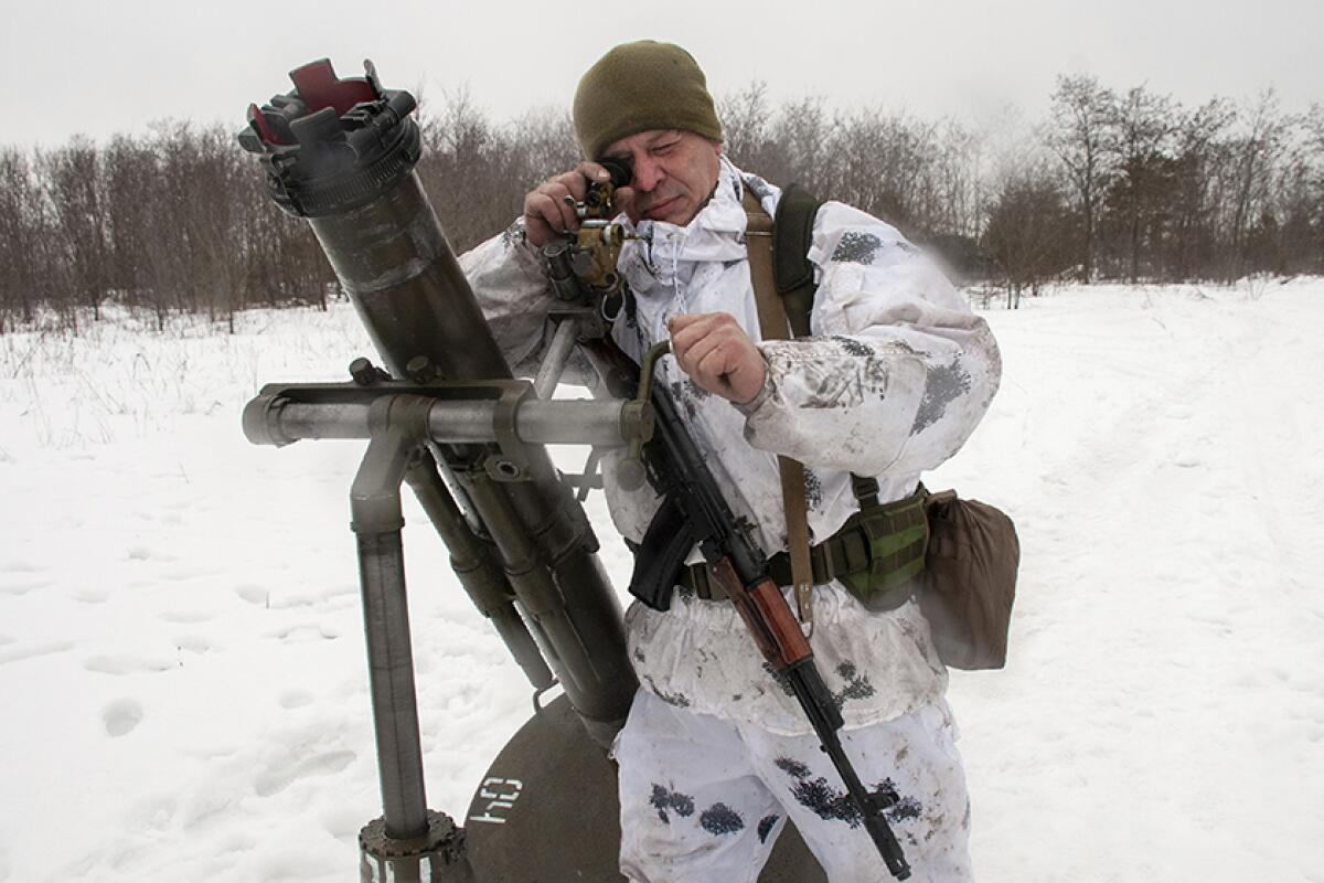A soldier stands by a weapon in the snow.