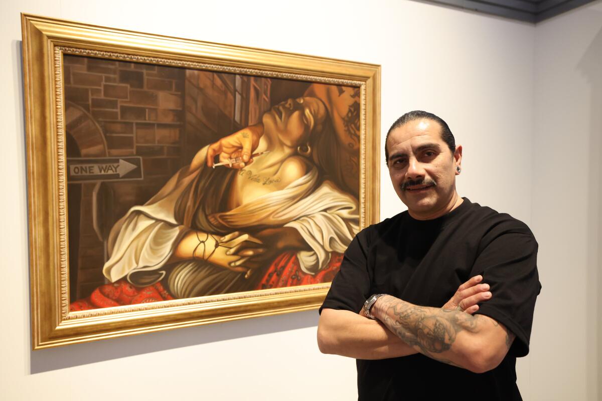 Artist Fabian Debora stands with arms folded in front of a painting of a woman leaning back with her eyes closed.