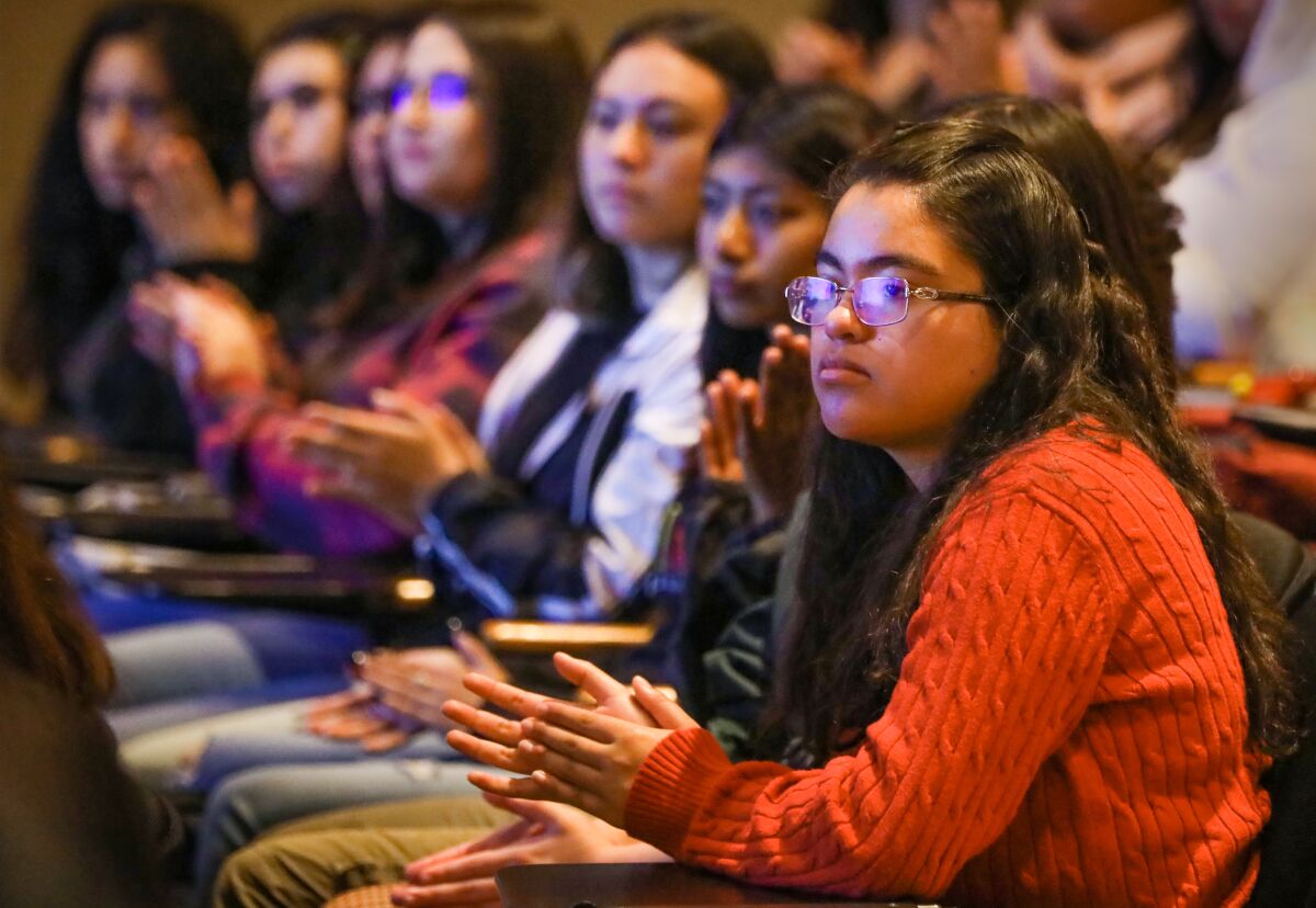 Students seated in an auditorium clap.