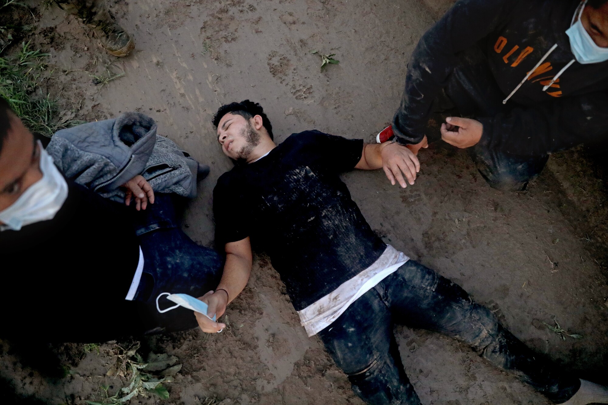 A man appearing exhausted lies on the ground and two men stand beside him