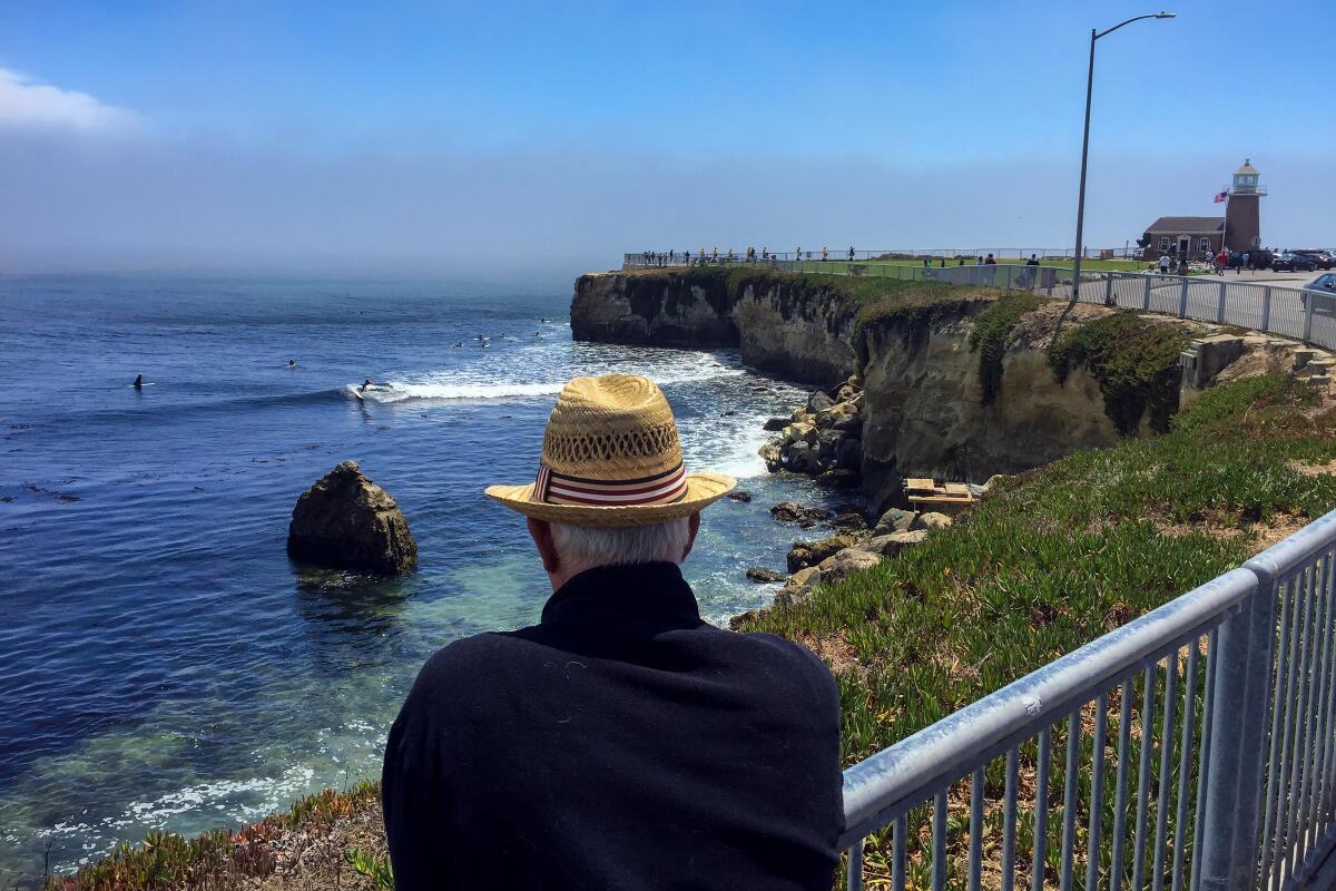 A man in a straw hat watches surfers ride waves at Steamer Lane.
