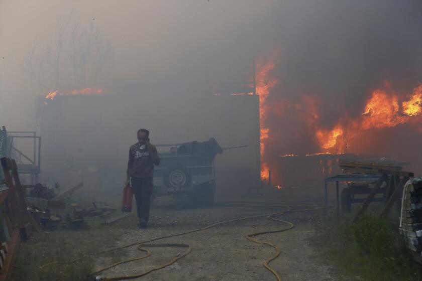 A man carries a fire extinguisher and seeks on the phone while a metalworking warehouse burns in Sever do Vouga, a town in northern Portugal that has been surrounded by forest fires, Monday, Sept. 16, 2024. (AP Photo/Bruno Fonseca)