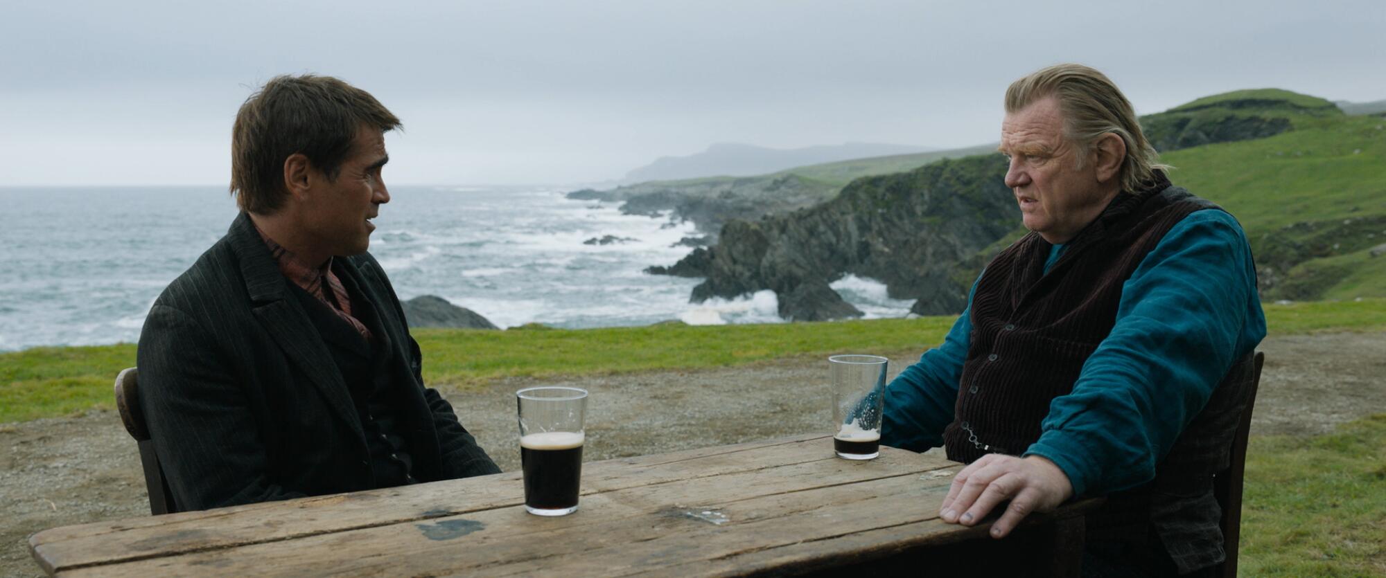 two men at a wooden table with beers by the sea 