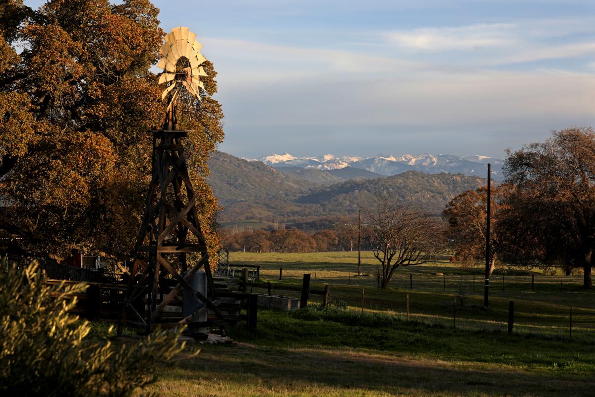 A weather vane stands in the foreground of a view of a valley with snow-capped mountains in the distance.