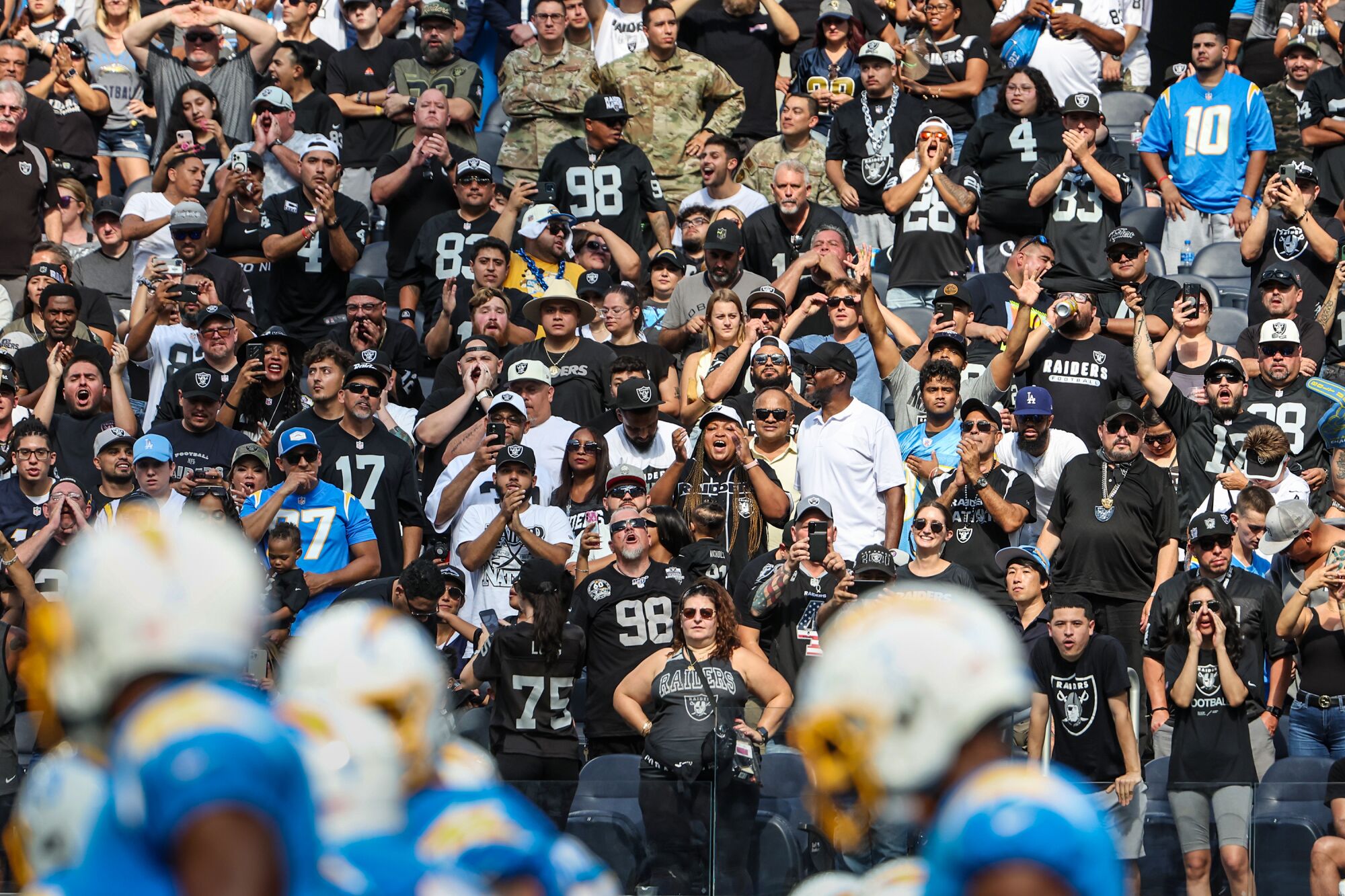 Os jogadores do Chargers se alinham perto da linha do gol enquanto uma multidão de fãs do Raiders mostra seu apoio ao time.