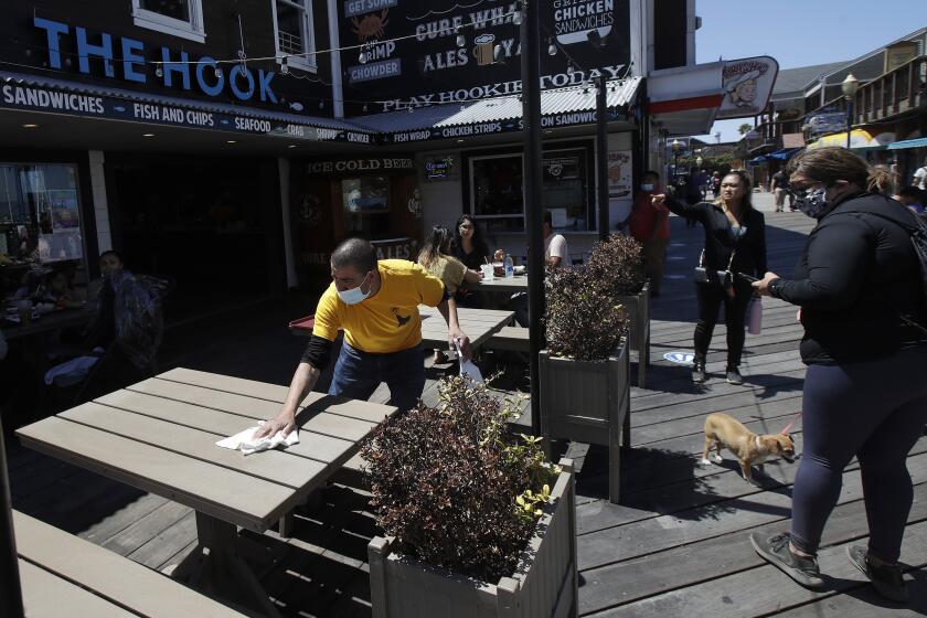 FILE - In this June 18, 2020, file photo, a man wears a face mask while cleaning an outdoor dining table at The Hook at Pier 39 in San Francisco. Restaurants and gyms are warning they cannot survive under California's new set of rules outlining when businesses can reopen during the coronavirus pandemic. Gov. Gavin Newsom announced a new, color-coded process Friday, Aug. 28, 2020, for reopening California businesses amid the coronavirus pandemic that is more gradual than the state's current rules to guard against loosening restrictions too soon.(AP Photo/Jeff Chiu, File)