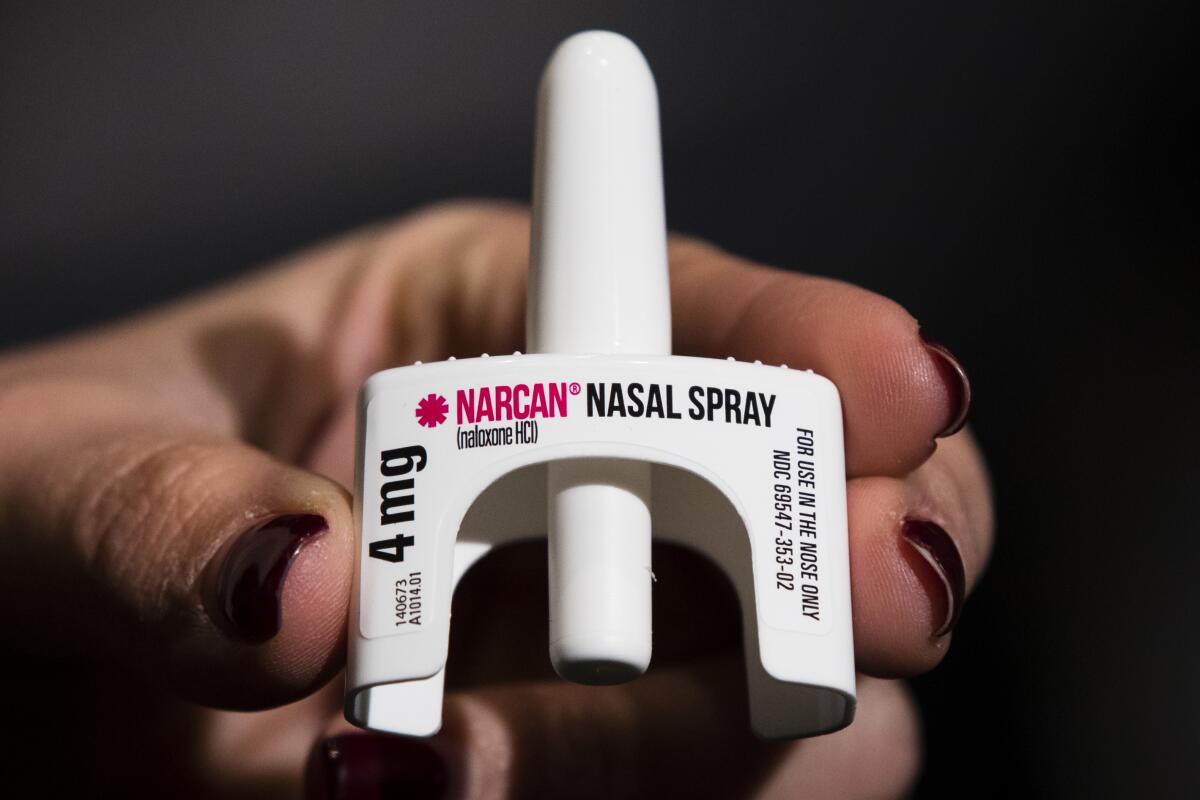 A close-up of a hand holding a white medication dispenser with the words Narcan nasal spray 4 mg 