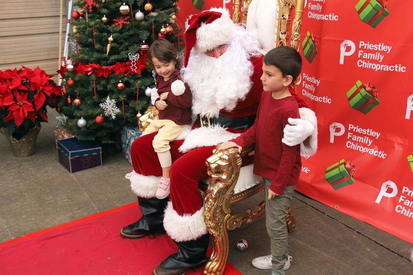 Eve, 2, left, and Remi, 5, of Newport Beach visit Santa provided by Priestly Family Chiropractic during the annual Corona del Mar Christmas Walk in the Corona del Mar Village along Pacific Coast Highway in Corona del Mar on Sunday, December 4, 2022. The Christmas walk is a holiday celebration with live entertainment, visits from Santa, beer and wine, vendor gifts and children activities. (Photo by James Carbone)