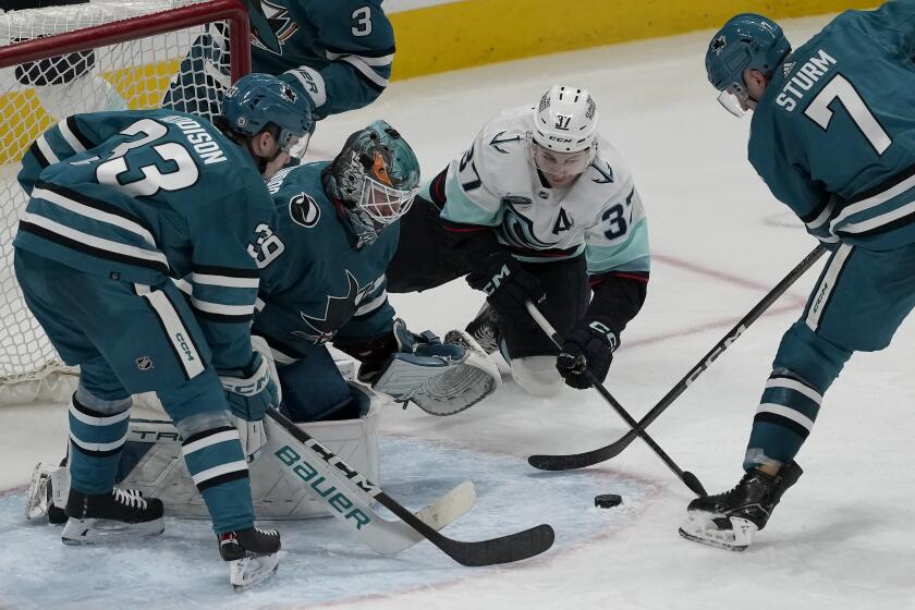Seattle Kraken center Yanni Gourde, middle right, reaches for the puck against San Jose Sharks defenseman Calen Addison, from left, goaltender Mackenzie Blackwood, middle left, and center Nico Sturm (7) during the third period of an NHL hockey game in San Jose, Calif., Monday, April 1, 2024. (AP Photo/Jeff Chiu)