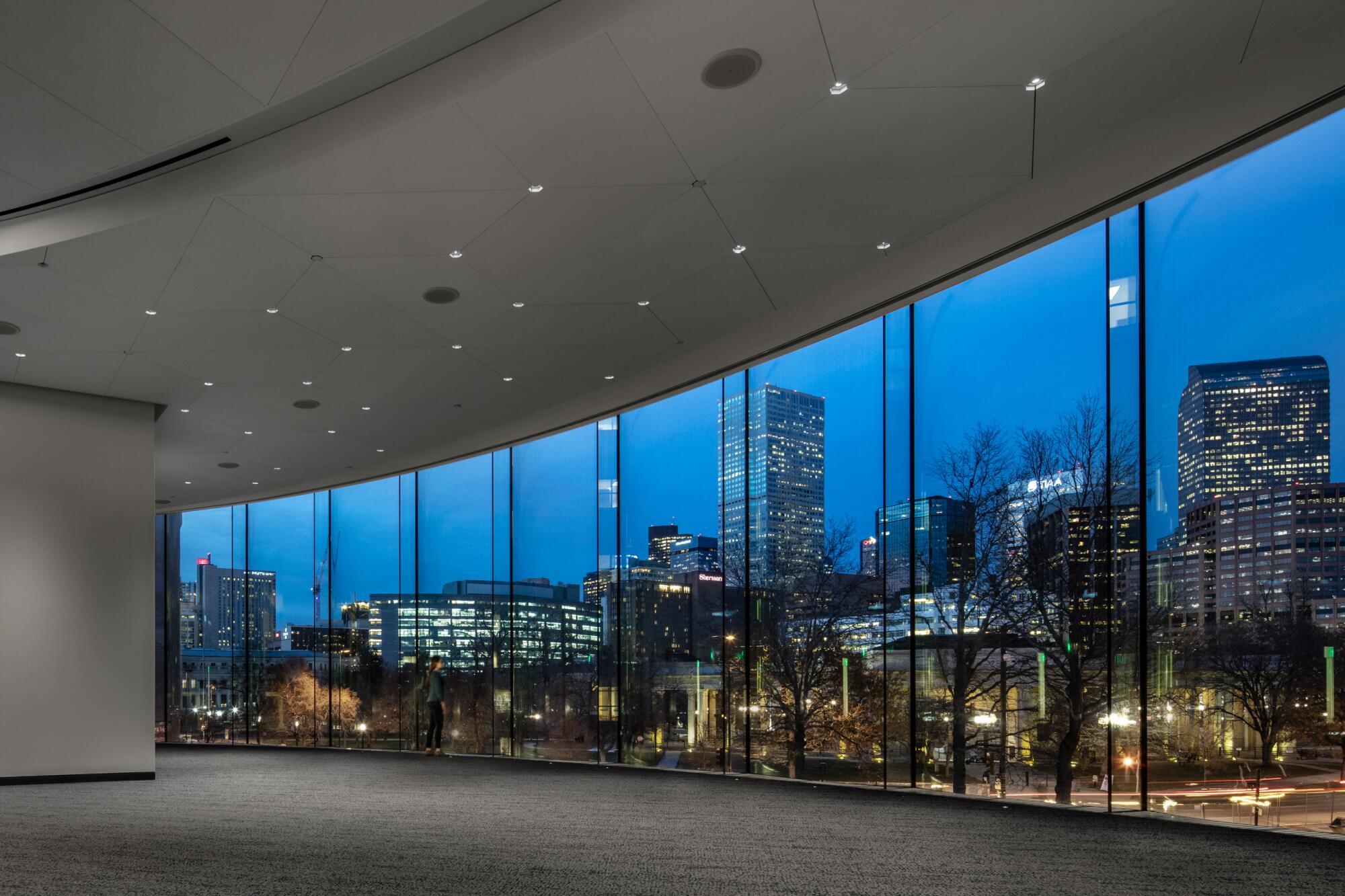The Denver skyline is seen through a series of floor-to-ceiling windows in the early evening